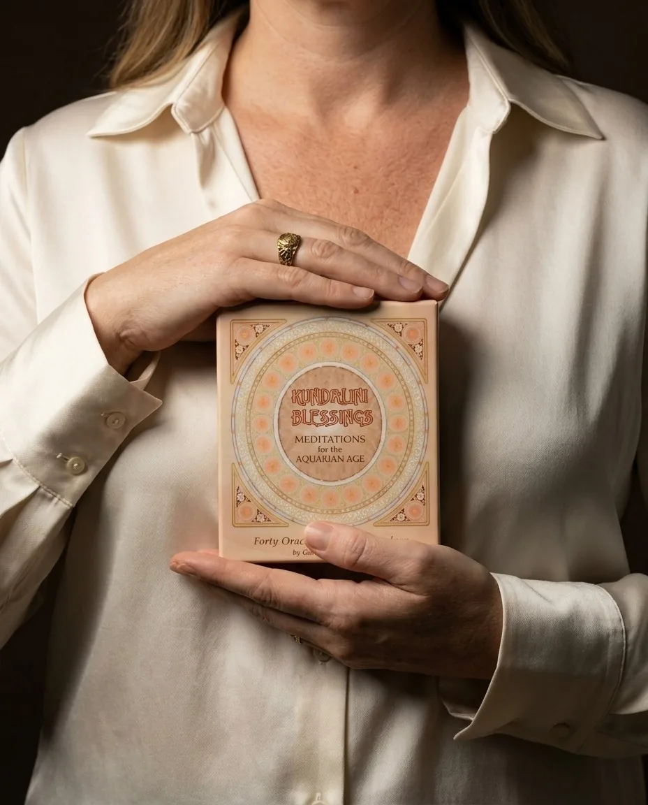 Hands holding the Kundalini Blessings deck in its box against an ivory silk shirt
